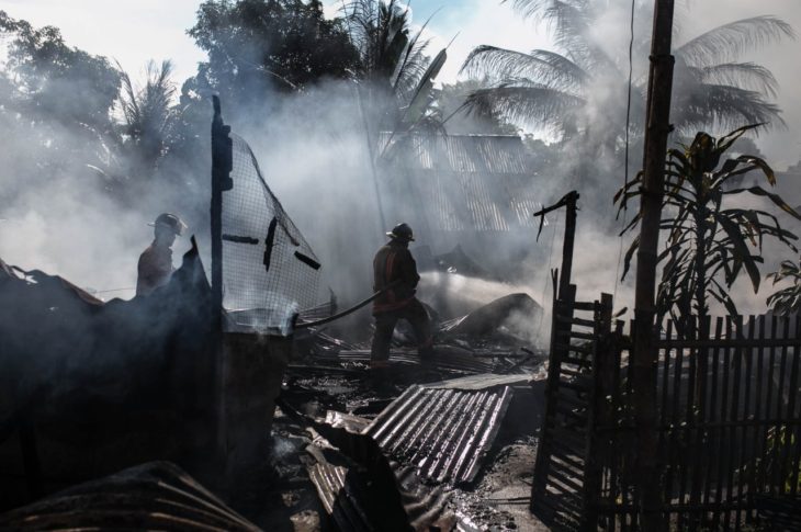 firefighter spraying water on a burnt house