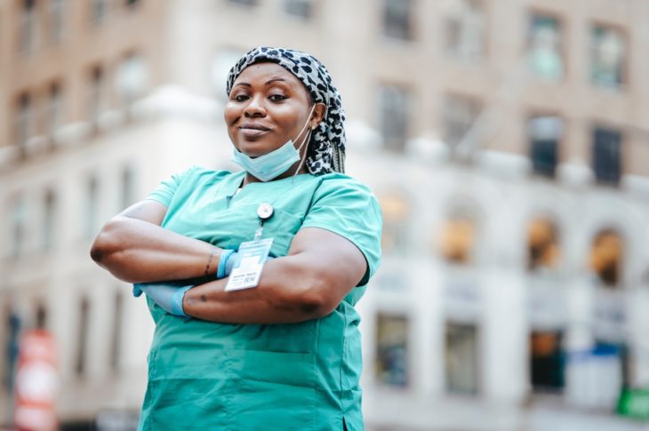 a nurse with her arms crossed smiling in the street